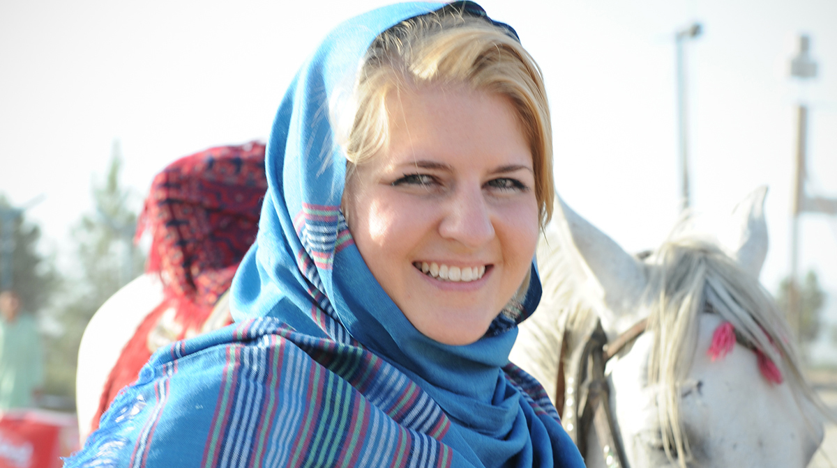 Lauryn Oates, wearing a blue head scarf, stands near a horse outside. 